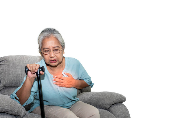 Asiatica donna anziana, seduta su un divano e detenendo walkers in casa, sono affetti da angina A causa di malattie cardiache, Su sfondo bianco isolato, alle persone pensionamento e concetto di assistenza sanitaria. - Foto, immagini