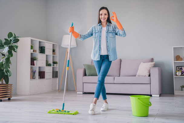 Full size photo of brunette millennial cool lady wash floor show okey wear jeans shirt sneakers gloves at home alone - Foto, imagen