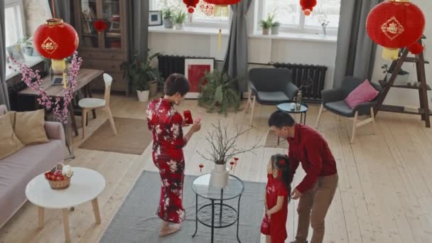 Alto angolo inclinazione verso il basso dei genitori asiatici e carina ragazza di 5 anni in abbigliamento tradizionale decorazione rami in vaso per il capodanno cinese - Filmati, video