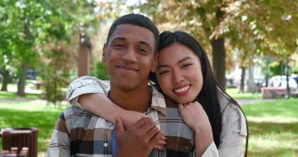 Concept of close relationships between two beautiful young beautiful multi-ethnic people. Woman and man hugging and stroking gently hand, cutely smiling looking at camera on the urban park background - Séquence, vidéo