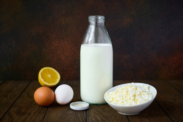 Dairy products, cottage cheese and milk, chicken eggs and lemon, dark background - Fotografie, Obrázek