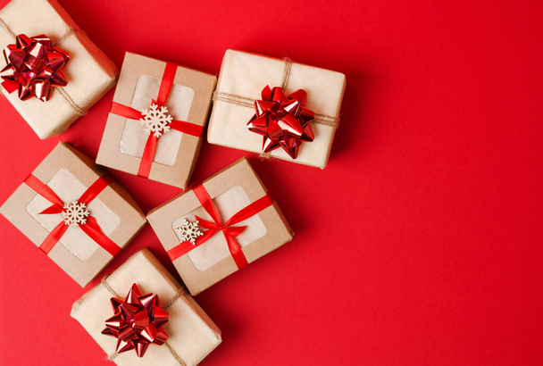Weihnachten, Neujahr. Geschenke in Kraftpapier und Kraftschachteln mit rotem Band und Schleifen auf rotem Hintergrund - Foto, Bild