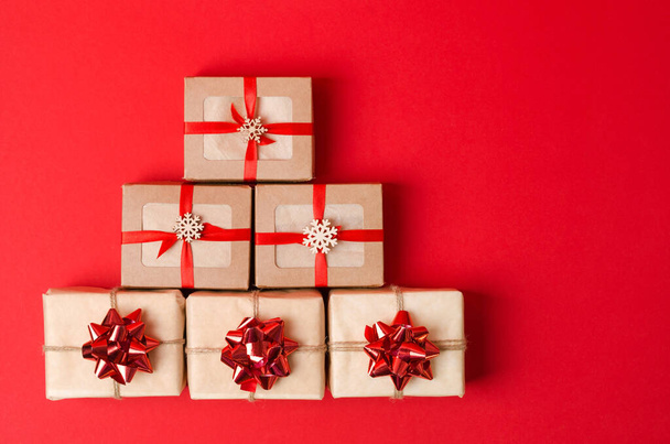 Новорічні подарунки викладаються у вигляді дерева на червоному тлі. Подарунки в крафткоробоках і крафт-папері з бантами
 - Фото, зображення