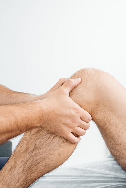 Ein Osteopath untersucht das Knie eines Mannes, der auf einer Massageliege liegt - Foto, Bild