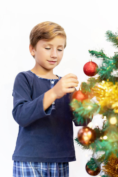 Šťastný chlapec v pyžamu zdobí vánoční stromek, dávat vánoční koule na to v chladném zimním ránu - Fotografie, Obrázek
