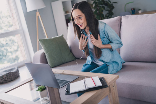 Portrait of attractive amazed cheerful woman sitting on divan using laptop calling talking having fun at home indoors - Foto, imagen