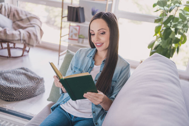 Portrait of attractive cheery focused woman lying on divan reading novel resting spending vacation at home indoors - Foto, Imagem