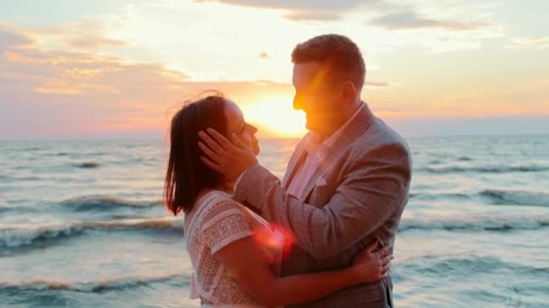 Любящая пара мужчин и женщин обнимаются и целуются у моря на закате. Обнимашки, поцелуи и чувственные отношения между молодыми людьми. Захватывающие закаты и солнечные лучи. - Кадры, видео