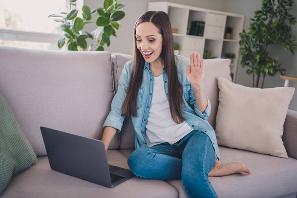 Portrait of attractive cheerful long-haired woman sitting on divan using laptop calling waving hi hello at home indoors - Foto, immagini