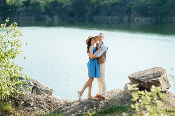 若い夫婦と女の子が花崗岩の岩に囲まれた山の湖の近くを歩いている - 写真・画像