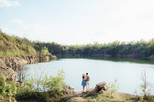 una pareja joven un chico y una chica están caminando cerca de un lago de montaña rodeado de rocas de granito - Foto, Imagen