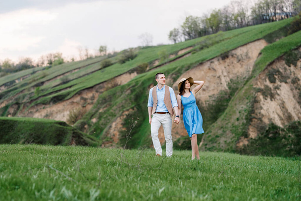 Ένα νεαρό ζευγάρι ένας άντρας και ένα κορίτσι περπατούν στους καταπράσινους λόφους του βουνού. - Φωτογραφία, εικόνα