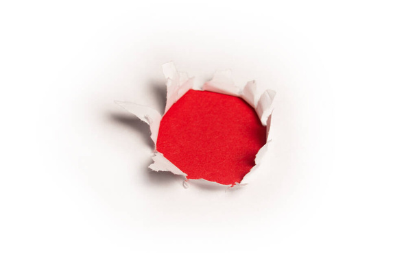 Un trou dans un papier blanc sur fond rouge, espace de copie.  - Photo, image