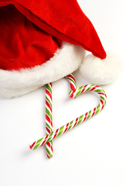 Two Candy Canes in Heart Shape and Santa Claus hat on White Background - vertical - Фото, зображення