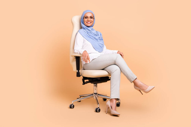 Full body photo of millennial east modern lady sit wear headscarf shirt eyewear pants stilettos isolated on beige background - Foto, Imagen