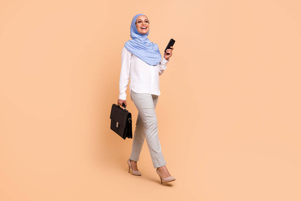 Full size photo of young east modern boss lady with bag telephone go wear headscarf shirt eyewear trousers high heels isolated on beige background - Φωτογραφία, εικόνα