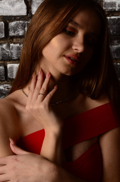 Een mooi jong meisje in een rode jurk in de studio. Luxe sieraden, kettingen en ringen, heldere make-up, rode lippen, manicure. Glamoureuze luxe dame. - Foto, afbeelding