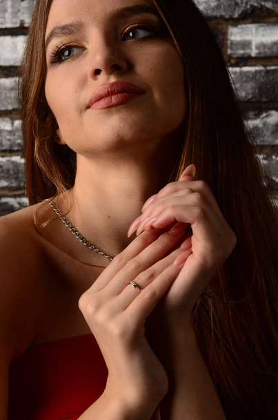 A beautiful young girl in a red dress in the studio. Luxury jewelry, necklaces, and rings, bright makeup, red lips, manicure. Glamorous luxury lady. - Foto, afbeelding