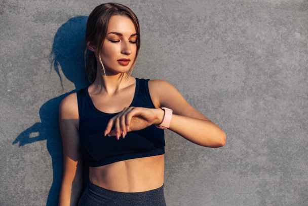 Fit woman looking at smartwatch and counting calories burned, Woman sitting relaxed after workout checking heart rate with smartwatch, Happy runner checking smartwatch after exercising outdoors - Foto, Imagen