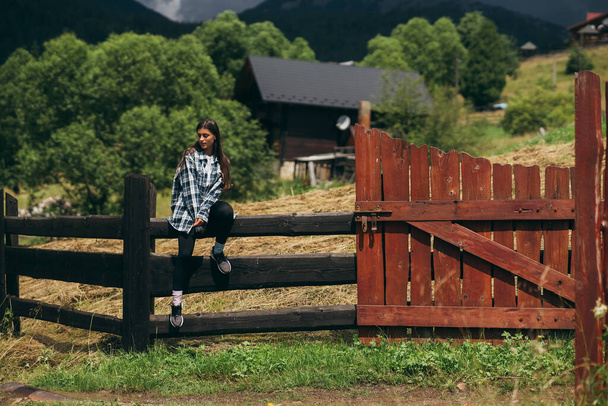 Молода приваблива кавказька жінка сидить на паркані. - Фото, зображення