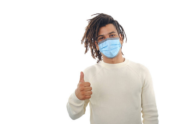 Man wearing a face mask and showing thumb up while standing against an isolated background. - Foto, imagen