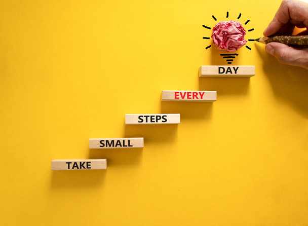 Take small steps every day symbol. Wooden blocks with words Take small steps every day. Beautiful yellow background, copy space. Businessman hand, light bulb. Business, step every day concept. - Photo, image