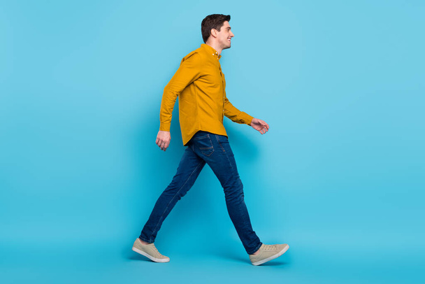 Full length profile photo of funny brunet boss man go wear yellow shirt jeans sneakers isolated on blue color background - Foto, Bild