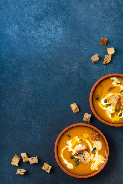Ready pumpkin cream soup with cream and croutons two servings on a blue background top view - Foto, afbeelding