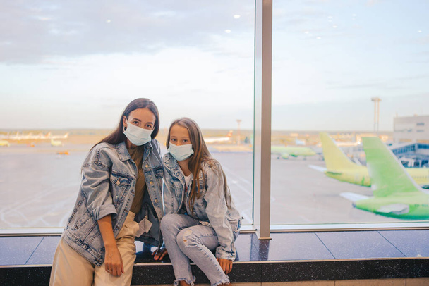Мать и девочка в медицинских масках в аэропорту. Защита от коронавируса и сцепления - Фото, изображение