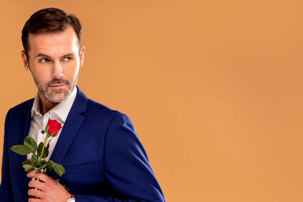 Handsome romantic man in suit holding one red rose in hand. Elegant look. Date. Real people lifestyle. A lot of copy space.  - Foto, afbeelding