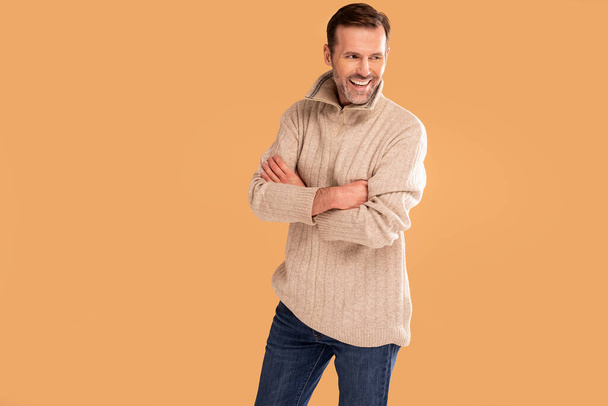 Handsome man with beard wearing casual sweater and jeans standing over studio background smiling. A lot of copy space. - Foto, afbeelding