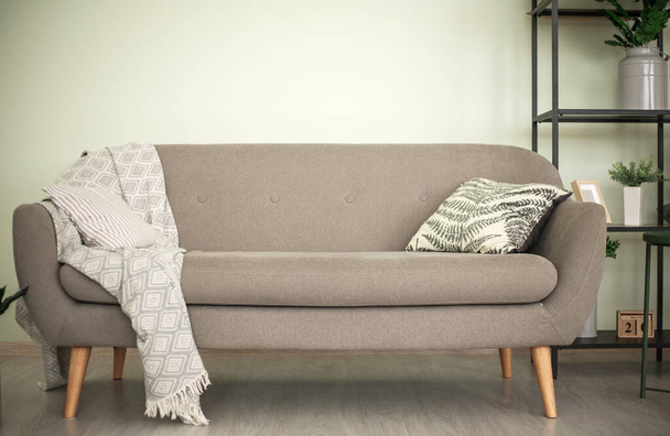Gray sofa with a pillow and a metal shelf with plants, against a wall background, minimalistic modern living room interior - Φωτογραφία, εικόνα