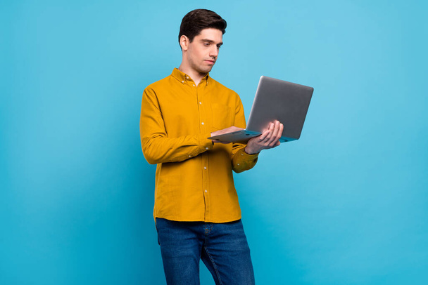 Photo of serious programmer guy hold laptop send email wear yellow shirt isolated blue color background - Фото, изображение