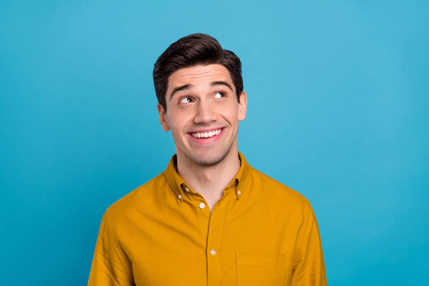 Photo of impressed dreamy young man wear yellow shirt looking empty space smiling isolated blue color background - Photo, Image
