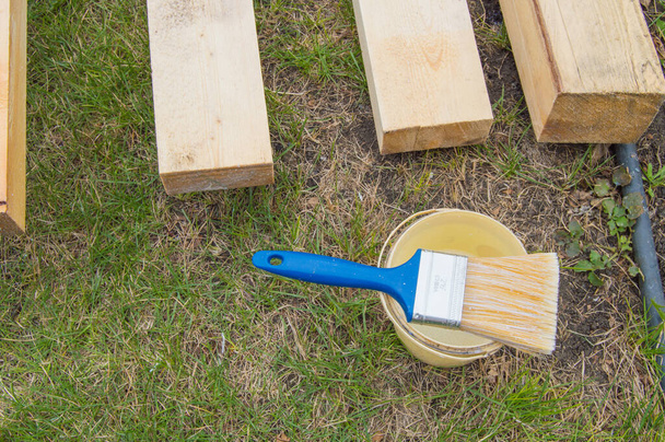 Příprava na natírání nových dřevěných prken ležících na trávě, štětec s vědrem. - Fotografie, Obrázek