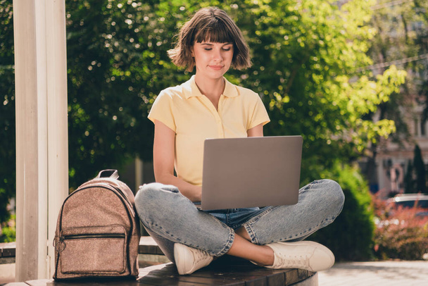 Portrait of attractive busy girl sitting on bench using laptop developing start-up project on fresh air outdoors - Φωτογραφία, εικόνα