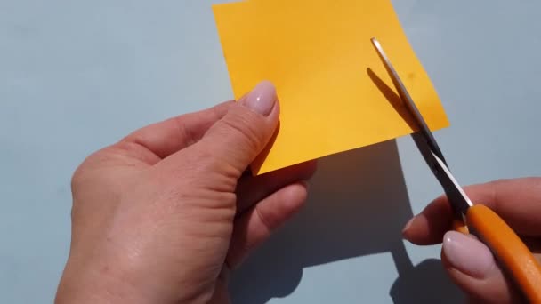 Vídeo 4k. Primer plano de las manos femeninas cortando papel naranja con tijeras pequeñas - Metraje, vídeo