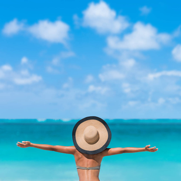 Beach summer holidays woman in happy freedom concept with arms up in happiness. Tourist vacation girl wearing fashion floppy sun hat carefree with copy space on blue sky. - Foto, Imagem