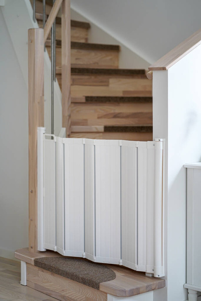 Белые пластиковые детские ворота безопасности на деревянной лестнице - Фото, изображение