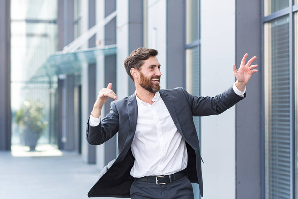 Cheerful happy business man dancing walk the city street background a modern office building outside, outdoors Funny successful businessman in suit celebtes victory - Фото, изображение