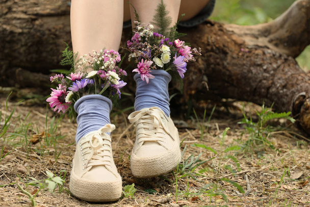Woman sitting on log with flowers in socks outdoors, closeup - Foto, Imagem