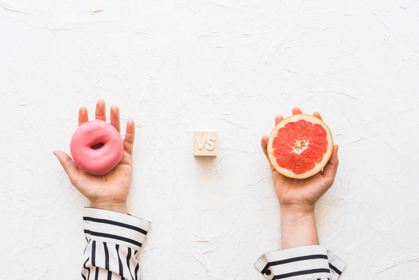 Frau Hand hält rosa Donut gegen Grapefruitscheibe texturierten Hintergrund. Hochwertiges Foto - Foto, Bild