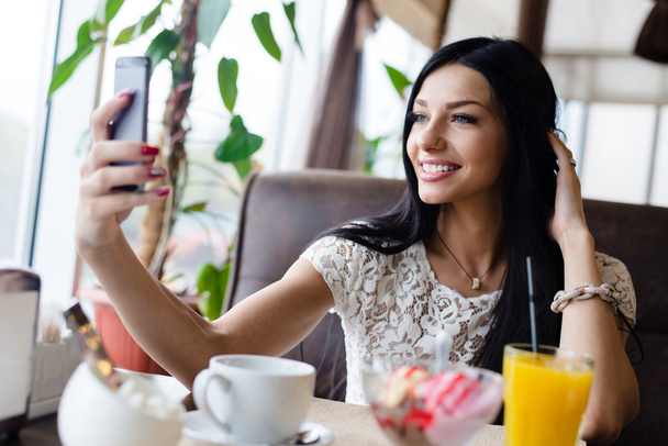 selfie étterem: Közelkép kép gyönyörű barna fiatal nő így selfy kép szórakozás boldog, mosolyog kávézóban háttér, mobiltelefon - Fotó, kép