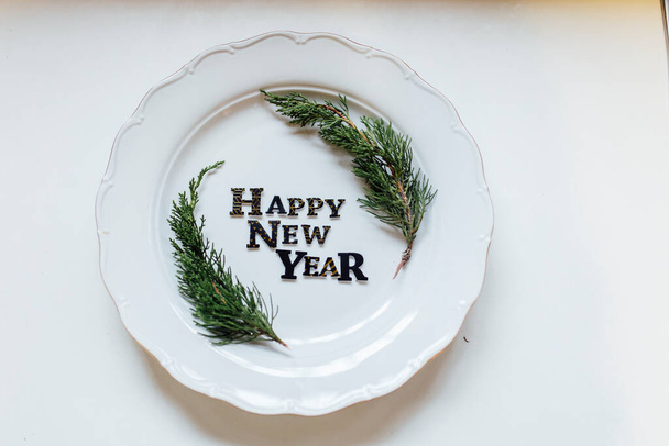 Happy New Year porcelain plate with Christmas wreath. Party decoration, flat lay, top view. Empty space. Restaurant menu concept. Isolated on white background. Winter holidays background. - Foto, immagini