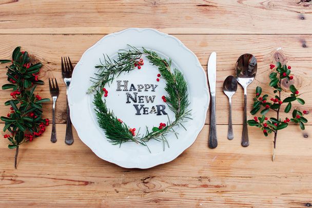 Happy New Year porcelain plate with Christmas wreath. Party decoration, flat lay, top view. Empty space. Restaurant menu concept. Isolated on wooden table background. Winter holidays background. - Fotoğraf, Görsel