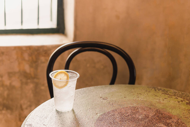 Copo de água espumante com fatia de limão na mesa com cadeira. - Foto, Imagem