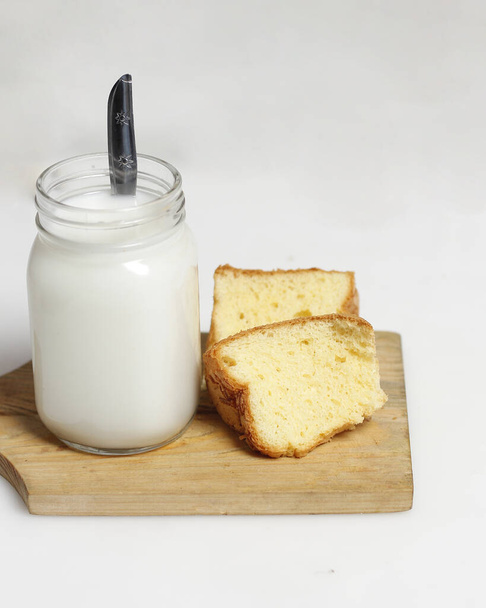 White milk drink served with bread is good for breakfast in the morning. This fresh cow's milk in addition to its sweet taste also contains many nutrients. warm milk in a glass cup. - Foto, imagen