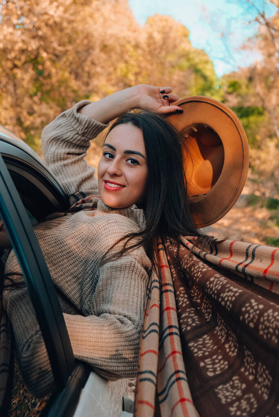 Brunette European looking cute girl sitting in a car enjoying sunny autumn weekend. Travel and road trip. Woman looking at the view from a car. Happy woman enjoying road trip - Foto, Bild