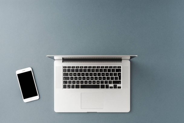 Overhead shot of laptop and bmobile phone on gray background. Office desktop - Фото, зображення