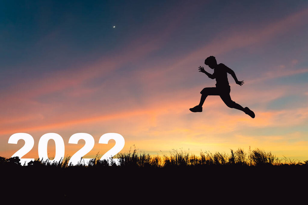 Al entrar en 2022 con confianza para tener éxito, Silhouette de un hombre saltando hacia la victoria. - Foto, Imagen